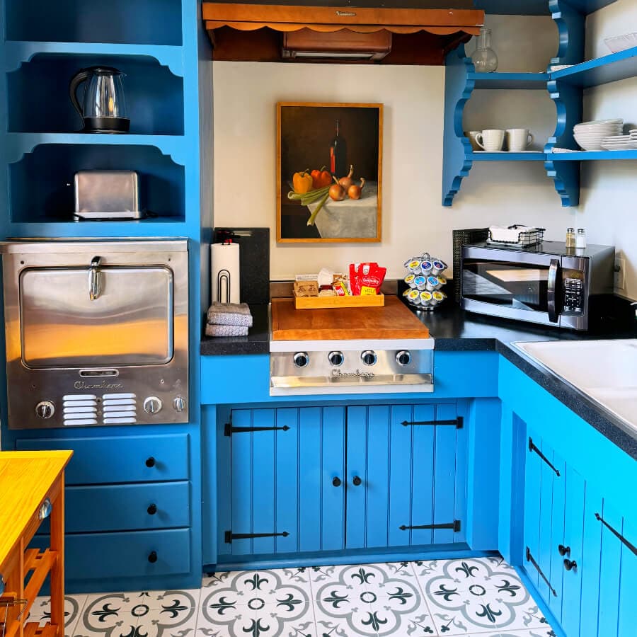 A bright blue kitchen featuring stainless steel appliances, a wooden countertop, and a colorful fruit painting on the wall.